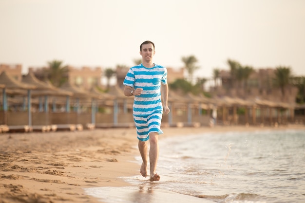 Hombre feliz corriendo a lo largo de la orilla de la playa