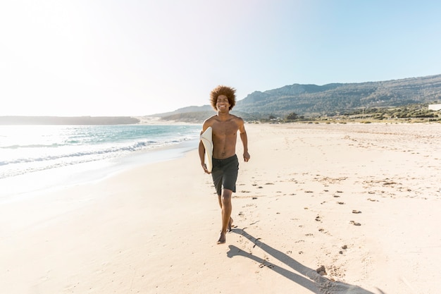 Hombre feliz corriendo por la playa con tabla de surf