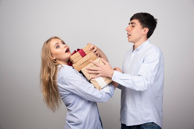 Hombre feliz dando cajas de regalo a su novia contra la pared gris.