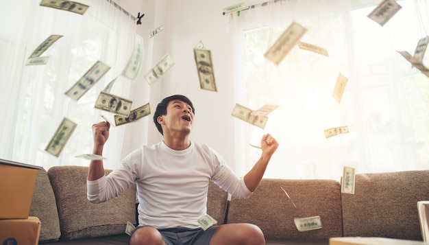 Hombre feliz con dinero en efectivo volando en la oficina en casa, rico del concepto de negocio en línea