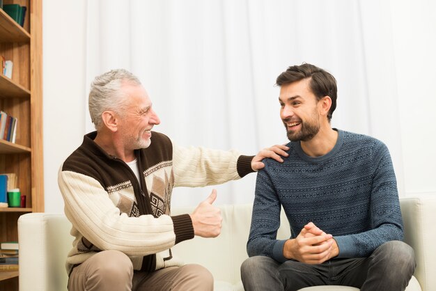 Hombre feliz envejecido con la mano en el hombro del chico joven en el sofá