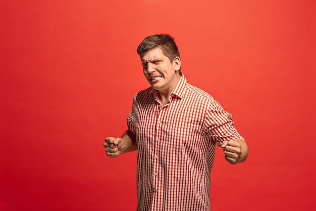 Hombre feliz de éxito ganador celebrando ser un ganador. Imagen dinámica del modelo masculino caucásico sobre fondo rojo de estudio.