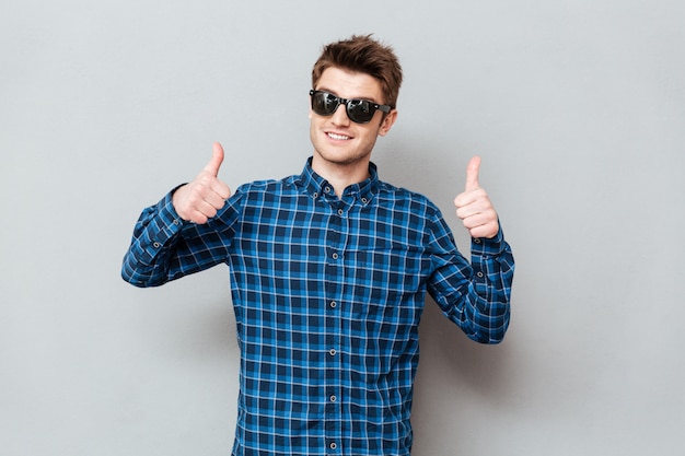 Hombre feliz con gafas de sol que muestran los pulgares para arriba.