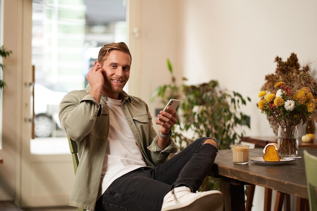 Hombre feliz y guapo en una cafetería escuchando música en auriculares inalámbricos se conecta al wifi de la cafetería para