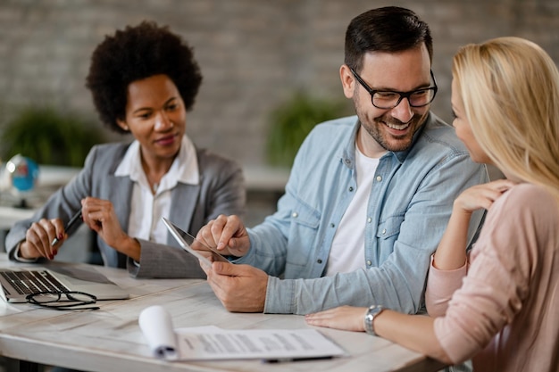 Hombre feliz hablando con su esposa mientras usa el panel táctil en una reunión con un agente inmobiliario en la oficina