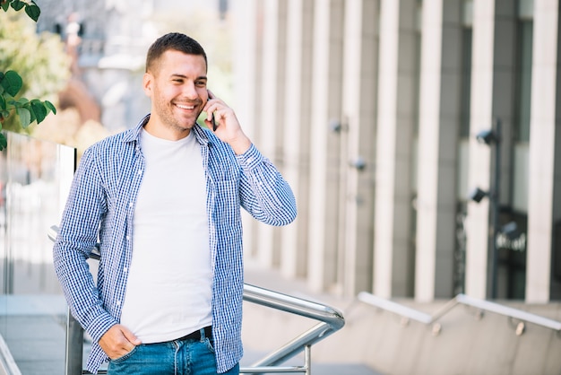 Hombre feliz hablando por teléfono cerca de barandilla