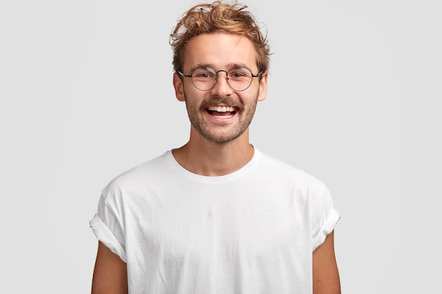 Hombre feliz hipster con sonrisa con dientes, viste camiseta blanca casual y gafas