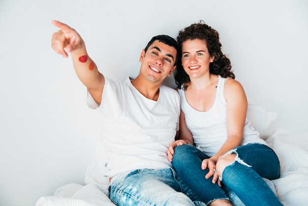 Hombre feliz joven con la mano estirada y la mujer que se sientan en cama