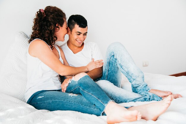 Hombre feliz joven y mujer que se sientan en cama