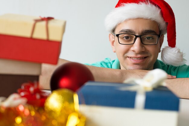 Hombre feliz en la mesa con regalos de Navidad y adornos