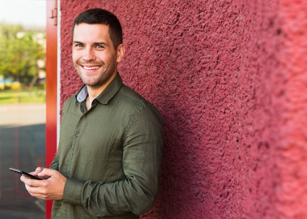 Hombre feliz mirando a la cámara mientras sostiene el teléfono móvil cerca de la pared roja