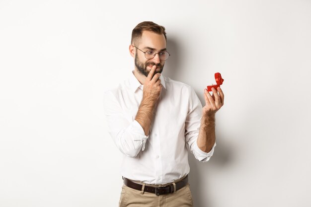 Hombre feliz mirando pensativo en anillo de bodas en caja, pensando en propuesta de matrimonio