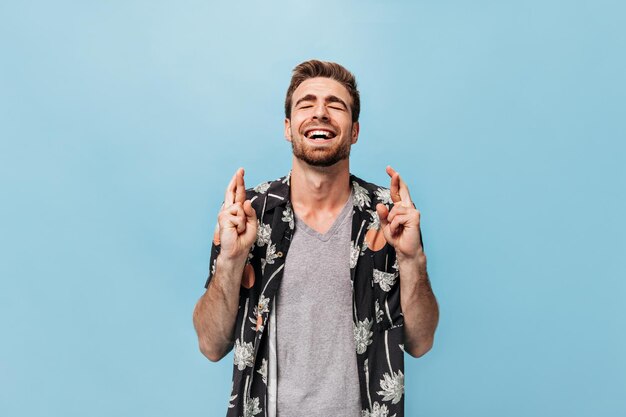 Hombre feliz de moda con peinado elegante y barba de jengibre en camiseta gris y camisa de manga corta de verano cruzando los dedos