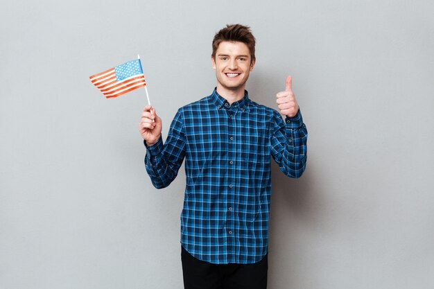 Hombre feliz mostrando los pulgares hacia arriba y sosteniendo la bandera de Estados Unidos.