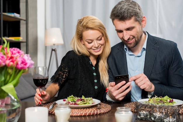 Hombre feliz y mujer alegre que usa teléfono inteligente en la mesa