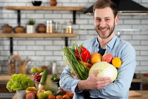 Hombre feliz de pie en la cocina con verduras crudas
