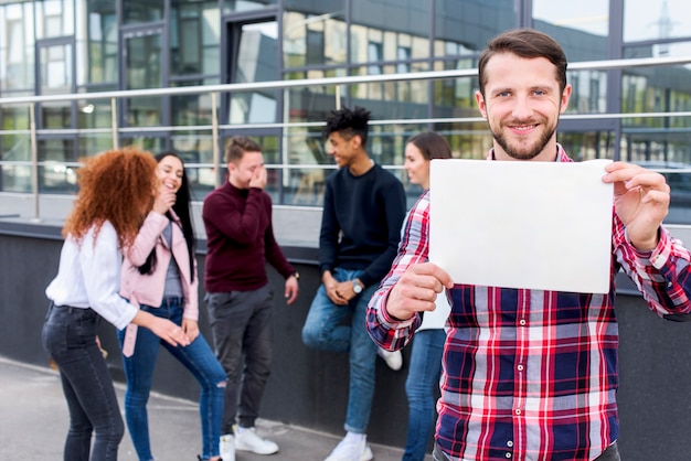 Hombre feliz de pie con sus amigos sosteniendo la tarjeta en blanco en sus manos