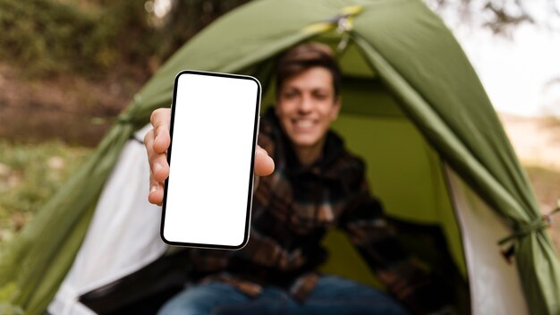 Hombre feliz que acampa en el teléfono móvil del espacio de la copia del bosque