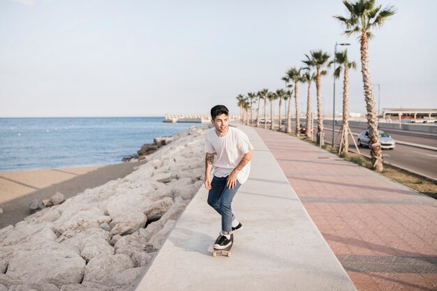 Hombre feliz que anda en monopatín cerca de la costa