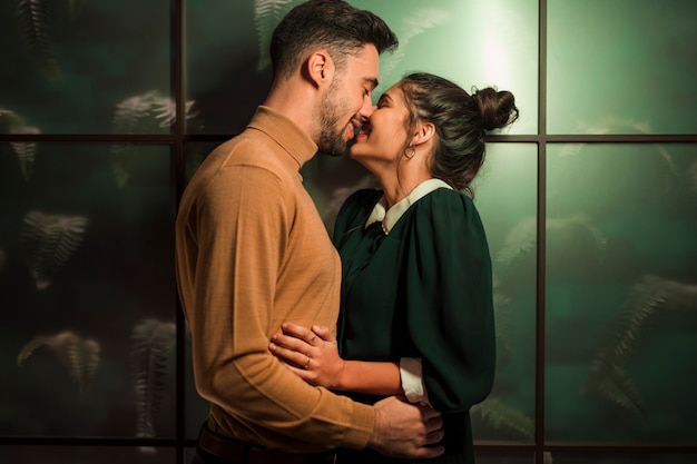 Hombre feliz que besa a la mujer alegre cerca de la pared