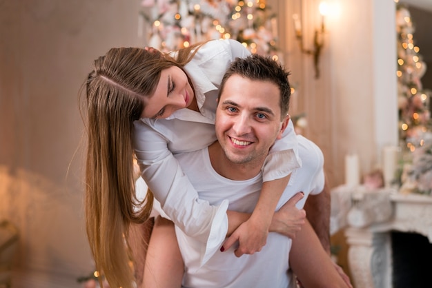 Hombre feliz que lleva a cuestas a la mujer con el árbol de navidad