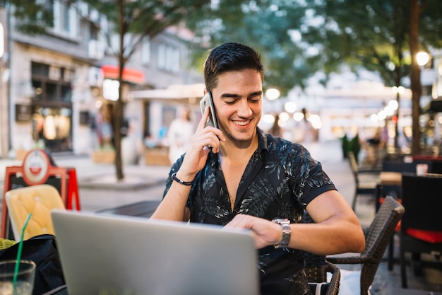 Hombre feliz que mira tiempo en el reloj mientras que habla en el teléfono móvil