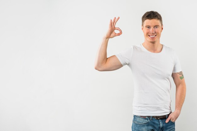 Hombre feliz que muestra la muestra aceptable contra el fondo blanco