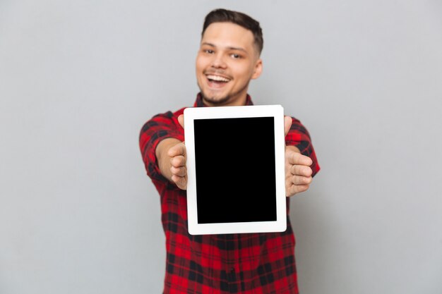 Hombre feliz que muestra la pantalla de la tableta en blanco en la cámara