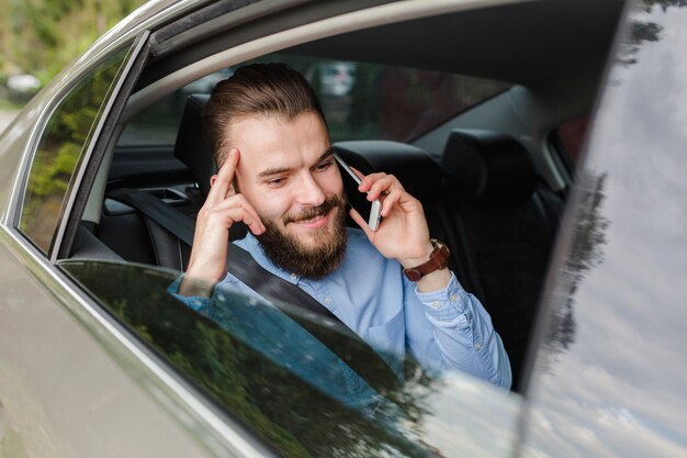 Hombre feliz que se sienta dentro del coche que habla en smartphone