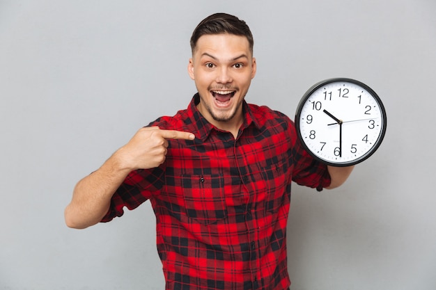 Foto gratuita hombre feliz que sostiene el reloj y apuntando a su