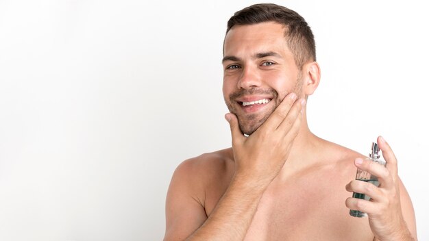 Hombre feliz rociando loción para después del afeitado de pie contra el fondo blanco.