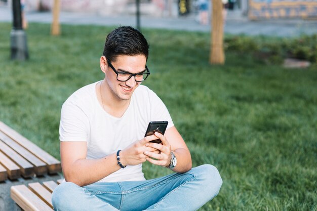 Hombre feliz sentado en la banca usando teléfono móvil