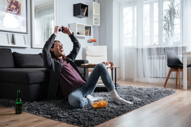 Hombre feliz sentado en casa en casa jugar con joystick