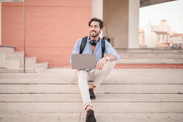 Hombre feliz sentado en la escalera con la computadora portátil