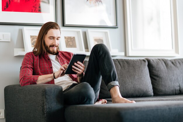 Hombre feliz sentado en el sofá y usando tableta en casa