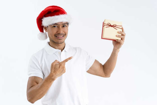 Hombre feliz con sombrero de Santa y apuntando a la caja de regalo