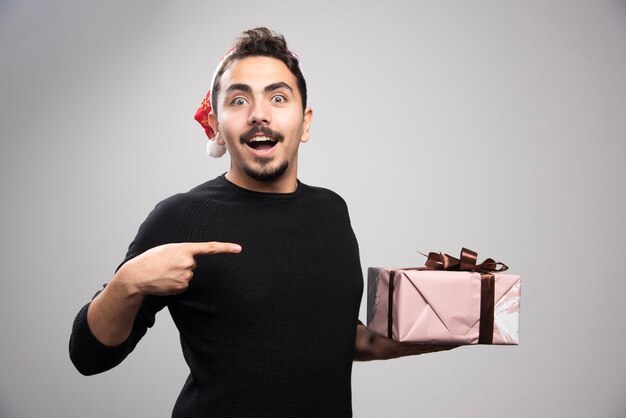 Un hombre feliz con un sombrero de Santa apuntando a un regalo.