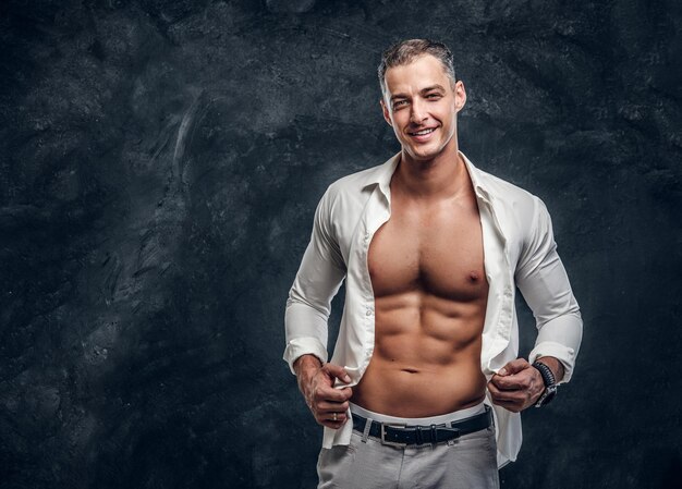 Un hombre feliz y sonriente con camisa blanca muestra su perfecto paquete de seis cuando abre la camisa.