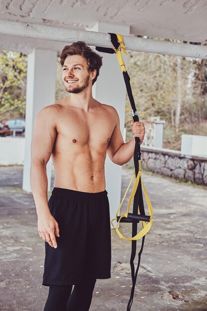 Un hombre feliz y sonriente con el torso desnudo sostiene vendajes especiales para su entrenamiento.