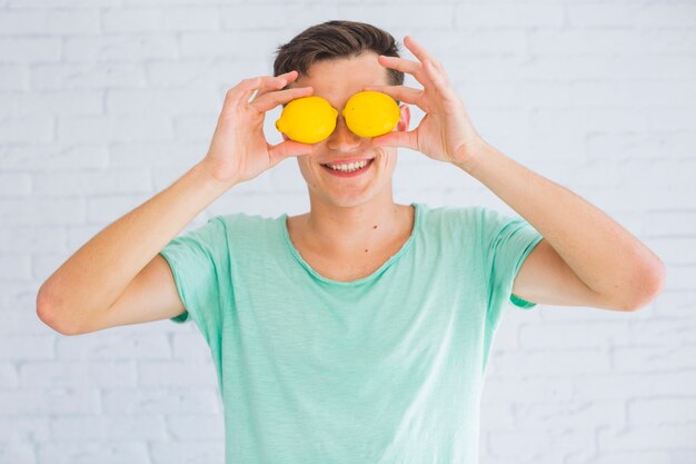 Hombre feliz sosteniendo limones enteros frente a sus ojos