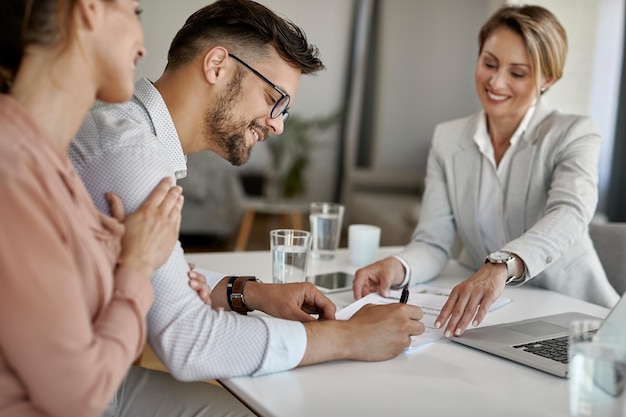 Hombre feliz y su esposa reuniéndose con un asesor financiero y firmando un acuerdo en la oficina