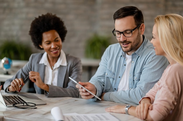 Un hombre feliz y su esposa usando una tableta digital mientras estaban en una reunión con el gerente del banco en la oficina