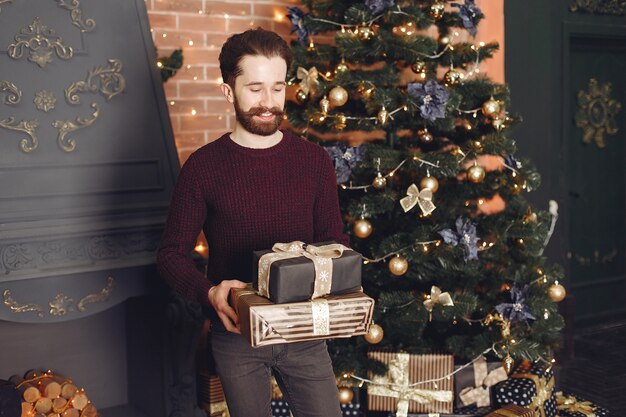 Hombre feliz en suéter rojo. Chico frente a la chimenea. Hombre en el fondo del árbol de Navidad.