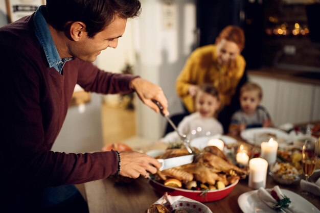 Hombre feliz tallando carne durante la cena de Acción de Gracias en la mesa de comedor