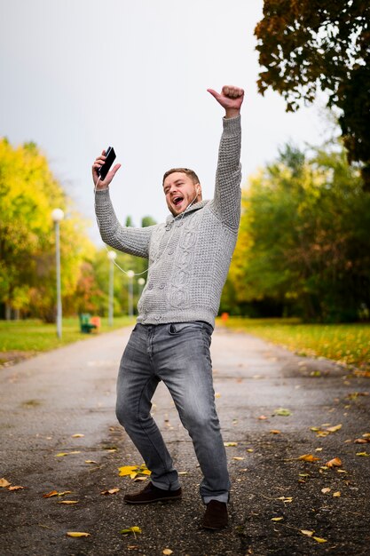 Hombre feliz con teléfono inteligente y auriculares en el parque