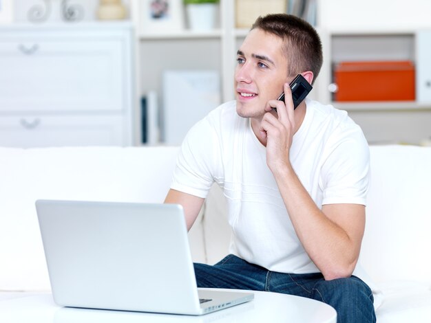 Hombre feliz con teléfono móvil y portátil en casa