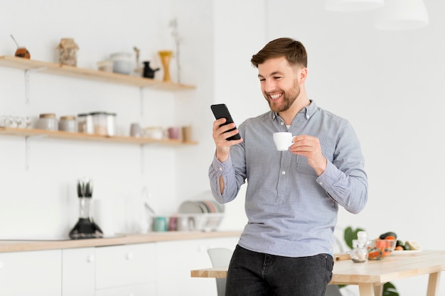 Hombre feliz tomando café mientras revisa el móvil