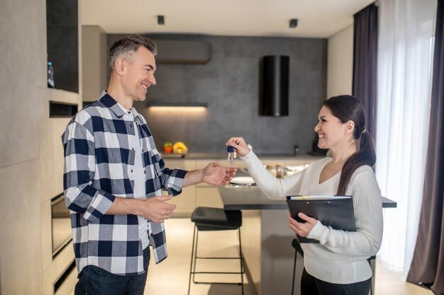 Hombre feliz tomando llaves de una mujer inmobiliaria de pie en el interior