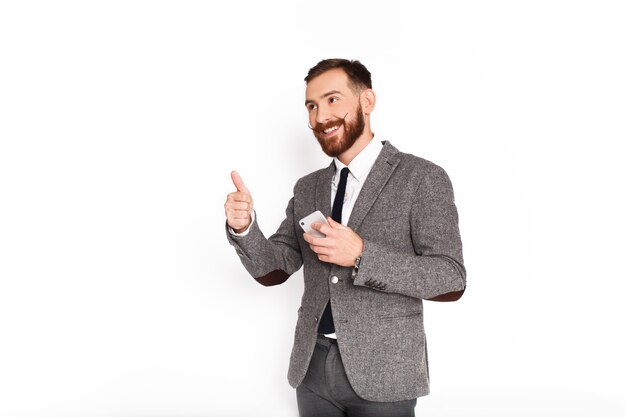 El hombre feliz en traje gris muestra el pulgar que sostiene smartphone en su brazo