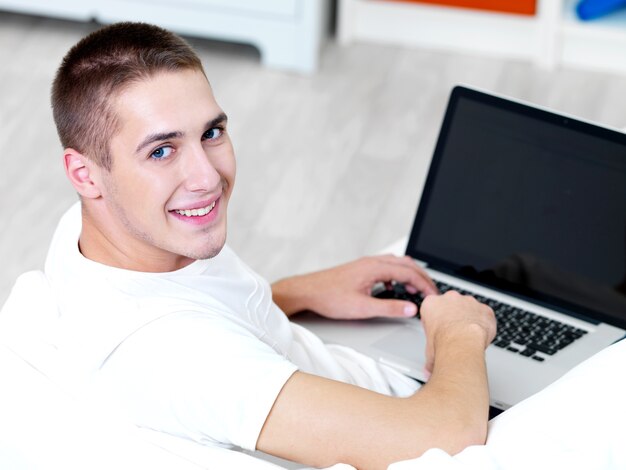 Hombre feliz usando laptop y acostado en el sofá